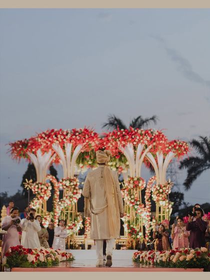 The groom walks towards the magnificent floral mandap, ready for the ceremony to begin. This shot captures the scale of the decor and the anticipation of the moment.