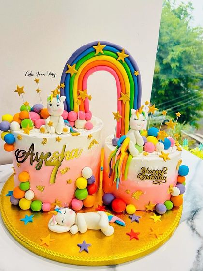 A double unicorn cake for a shared celebration, complete with rainbows, stars, and colorful decorations.