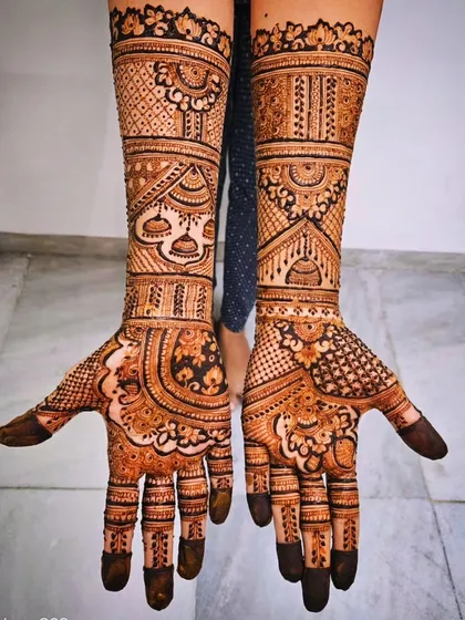 This bridal design features hanging 'jhumka' (earring) motifs on the arms, a popular and elegant choice. The palms are filled with dense, traditional patterns for a complete look.