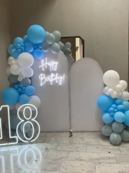 A clean and modern 18th birthday setup with white arched backdrops and a blue and white balloon arrangement.