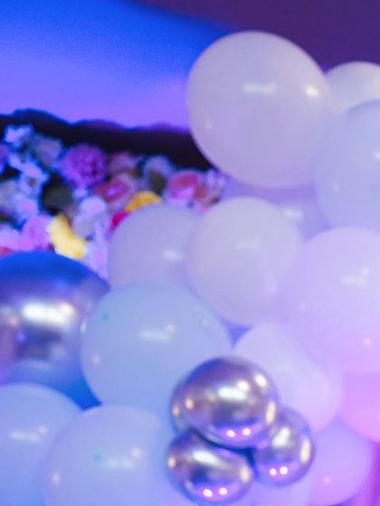 A beautiful arrangement of white, silver, and blue balloons with floral elements, part of an elegant party decor setup.