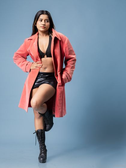 A full-length fashion portrait against a cool blue background. The composition uses negative space to draw attention to the model and her confident stance.