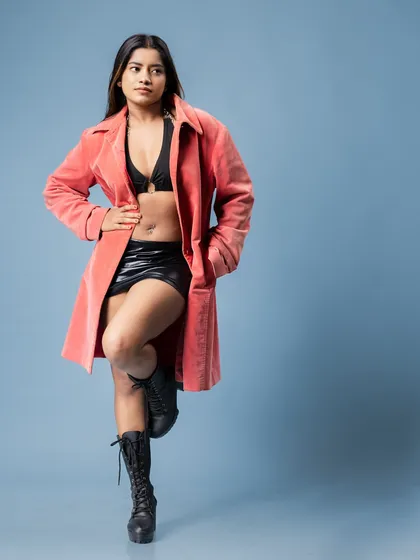 A full-length fashion portrait against a cool blue background. The composition uses negative space to draw attention to the model and her confident stance.