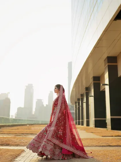 A side profile of the bride against a city skyline, her red lehenga vibrant against the modern background.