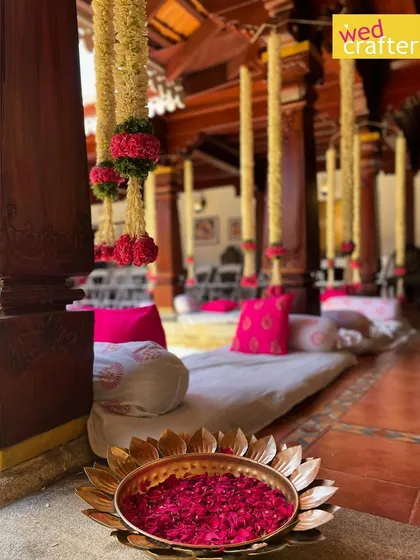 Low-angle seating with plush pink pillows arranged in the heritage courtyard, with hanging floral decor and a brass bowl of petals in the foreground.