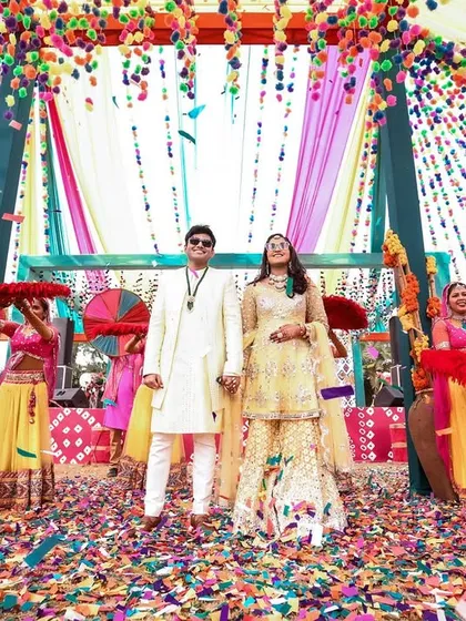 The couple stands proudly amidst a sea of confetti, the colorful draped ceiling and energetic dancers creating a perfect carnival atmosphere.