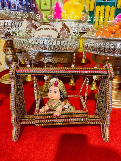 A close-up of a beautifully decorated miniature cradle with a baby doll, a charming centerpiece for a Naming Ceremony. You can also see the personalized coconuts in the background.