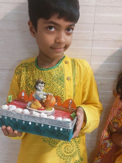 A young participant in his festive kurta, proudly holding the Krishna singhasan (throne) he decorated during our Janmashtami workshop.