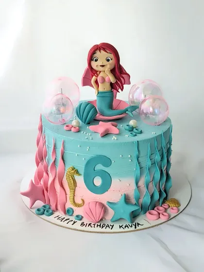 A lovely mermaid cake in shades of teal and pink. The design features buttercream waves, edible shells, a seahorse, and a beautiful mermaid topper.