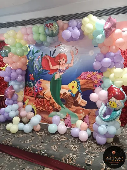 A beautiful 'The Little Mermaid' themed photo corner with a character backdrop and a pastel balloon arch.