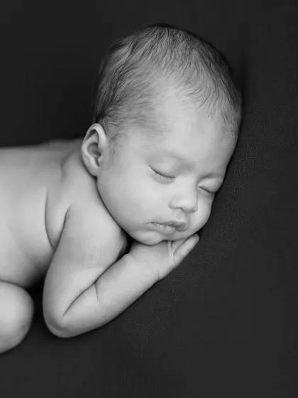 A timeless black and white portrait of a newborn sleeping on their side. The focus on form and shadow creates a powerful and artistic image.