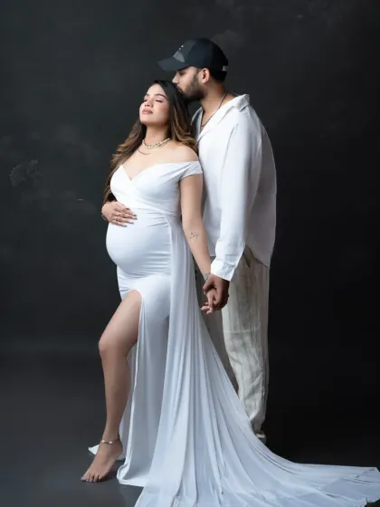 A stylish and romantic pose. The couple, dressed in white, shares a quiet moment, their hands connected as they anticipate their new arrival.