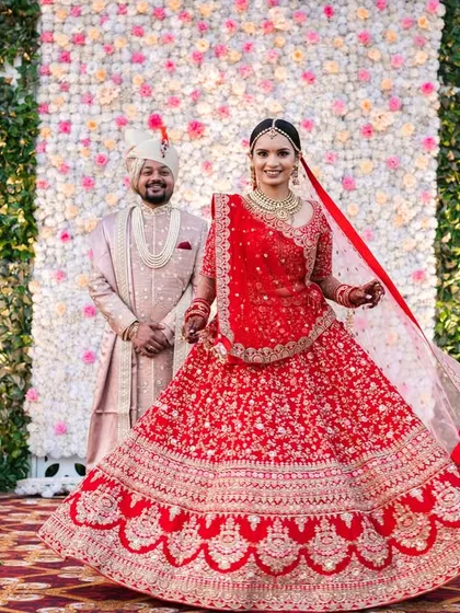 A beautiful twirl shot of the bride, showing off her magnificent red lehenga against the floral backdrop of the mandap.