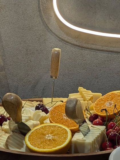 A close-up of a cheese board under soft neon lighting. This shot highlights the vibrant colours of fresh cherries and oranges against a selection of artisanal cheeses.