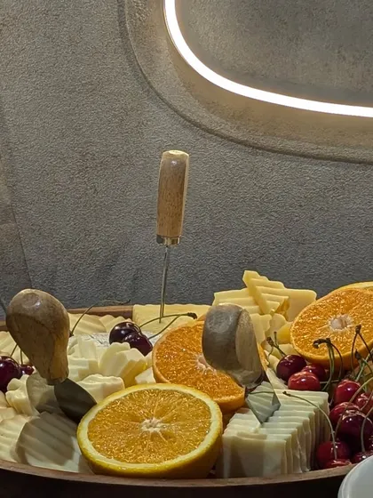 A close-up of a cheese board under soft neon lighting. This shot highlights the vibrant colours of fresh cherries and oranges against a selection of artisanal cheeses.
