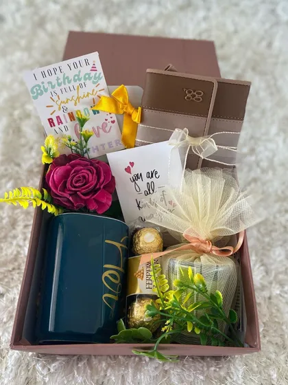 A cheerful and elegant birthday gift box for her. This hamper features a "Her" mug, a wallet, Ferrero Rocher chocolates, a scented candle, and a lovely birthday card wishing a day full of sunshine, rainbows, and love.
