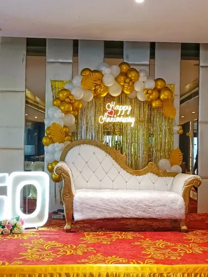 I create special setups for milestone celebrations, like this 50th wedding anniversary. The stage features a gold and white balloon arch, a 'Happy Anniversary' neon sign, and large, illuminated '50' numbers for a perfect photo opportunity.