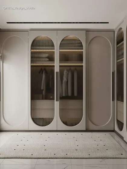 This image highlights a bespoke walk-in wardrobe I designed to blend elegance with functionality. The use of fluted glass in the arched doors offers a glimpse of the organized interior while maintaining a sense of privacy, and integrated lighting turns clothing storage into a beautiful display.