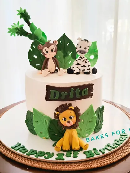 A jungle animal-themed cake with handcrafted fondant figures of a lion, zebra, and monkey. The simple white background makes the cute characters pop.