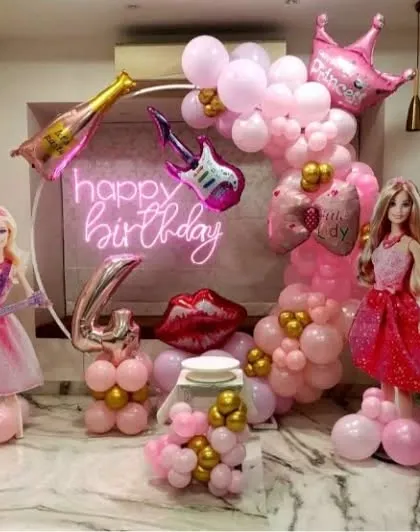 A rockstar Barbie theme for a 4th birthday. This glamorous pink setup includes Barbie doll props, a neon sign, and foil balloons shaped like a guitar and lipstick.