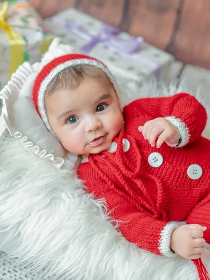 A beautiful, bright-eyed portrait of a newborn nestled in a basket. The soft fur and festive red outfit create a warm and adorable image.