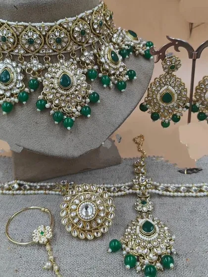 A close-up of a green Kundan choker set with matching earrings, maang tikka, and nath.