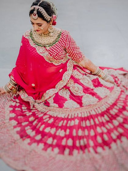 A beautiful portrait of the bride, Anjali, seated and showcasing the full spread of her stunning pink bandhani lehenga.