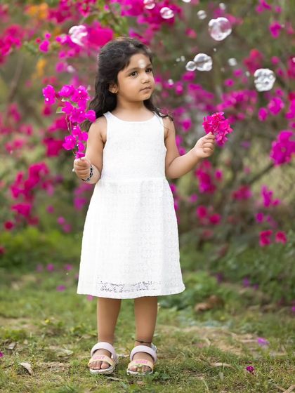 A whimsical outdoor photo of a little girl in a white dress, surrounded by bubbles and bright pink bougainvillea. We use simple props like bubbles to bring out genuine wonder and smiles.