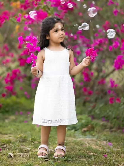A whimsical outdoor photo of a little girl in a white dress, surrounded by bubbles and bright pink bougainvillea. We use simple props like bubbles to bring out genuine wonder and smiles.