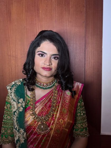 A classic portrait of bride Roopa. The makeup features a soft smokey eye and a defined lip, creating a sophisticated look that complements her traditional green and pink saree.