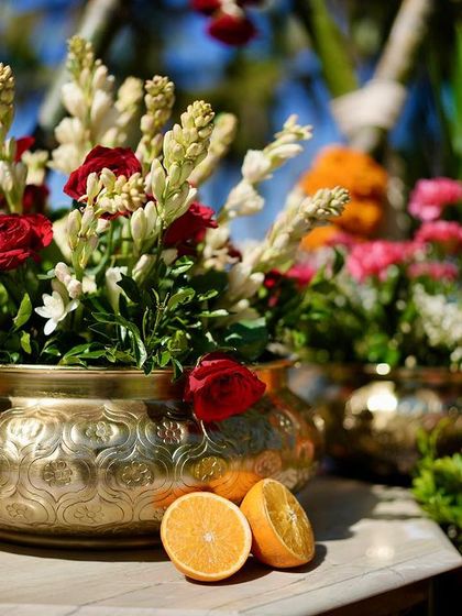 A beautiful brass pot filled with red roses and white tuberoses, with fresh oranges adding a pop of color and a nod to the Malabari theme.