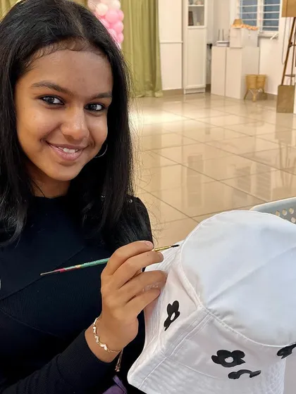 This participant is painting delicate black flowers on her hat, creating a chic and stylish design.