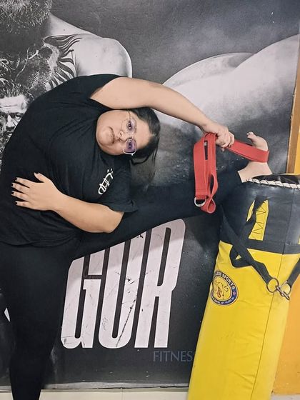 A student using a yoga strap and a punching bag for support in a deep side stretch. This creative use of props helps to open the side body and hips.