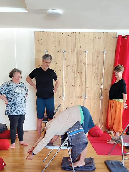Demonstrating a supported forward bend to a class. The chair allows for a gentle release of the spine and hamstrings, making it a restorative and therapeutic variation.