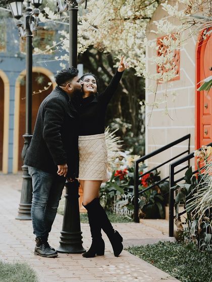 A sweet, candid moment with the groom kissing the bride's cheek as she points upwards, set in a charming park.