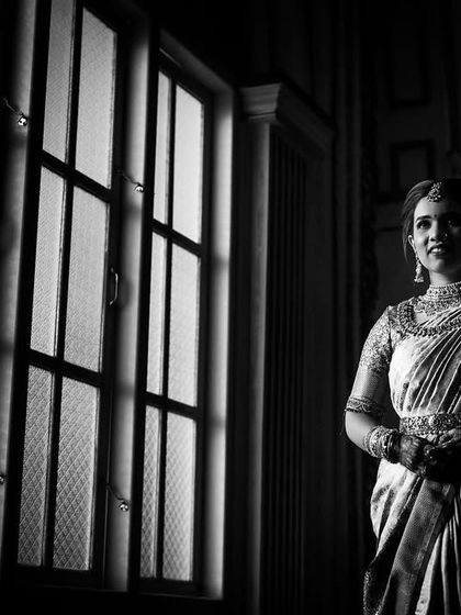 A classic black and white bridal portrait. The bride stands near a window, the soft light creating a timeless and elegant mood.