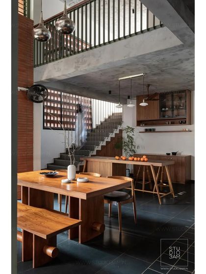 The open-plan dining and kitchen area in the 'Olive Dwelling' features custom wooden furniture and a double-height space that connects to the upper floor.