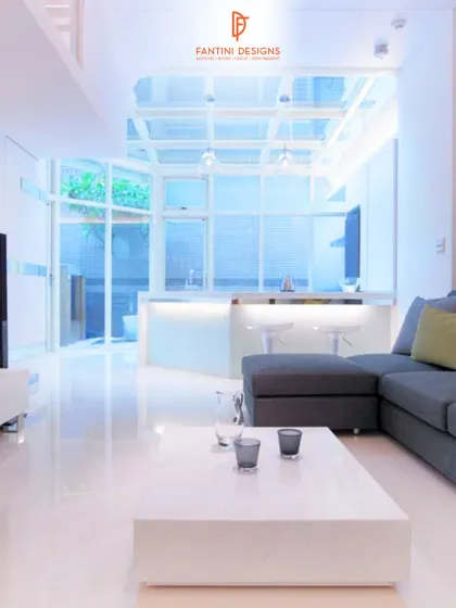 A wide shot of the living room, showing the open-concept layout that connects to the kitchen and an outdoor space. The polished white floors enhance the sense of space.
