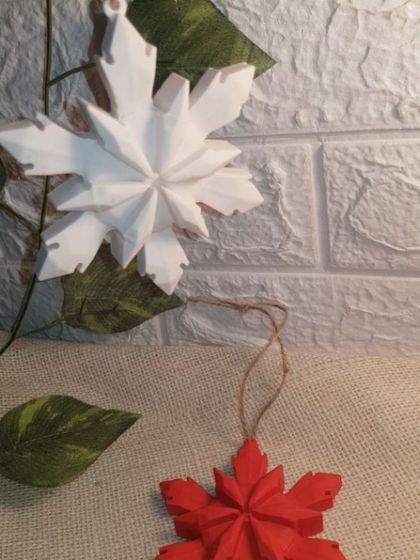 The white 3D Snowflake Ornament, contrasted with the red one. We provide natural twine for hanging, which complements the handmade, earthy feel of the Jesmonite.