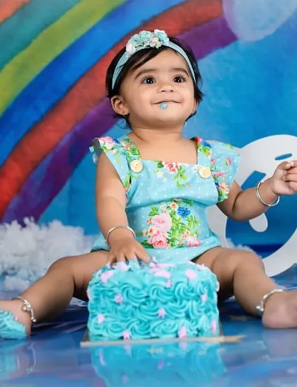 A rainbow-themed cake smash for a bright and cheerful first birthday. Her happy expression says it all as she digs into her turquoise cake.