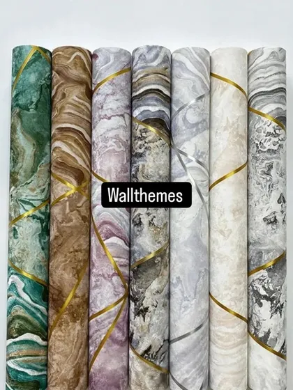 A collection of modern wallpaper rolls with marble-effect geometric patterns and gold accents. This shows the variety of colors available, from green and brown to grey and white.