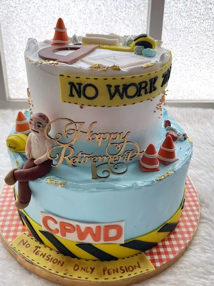 A two-tier retirement cake for a civil engineer from CPWD. The design features blueprints, a hard hat, and a funny caricature, celebrating the end of a long career.