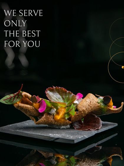 We serve only the best. This appetizer features a crispy, cone-shaped shell filled with a vibrant mixture and garnished with edible flowers and microgreens, served on a modern slate platter.
