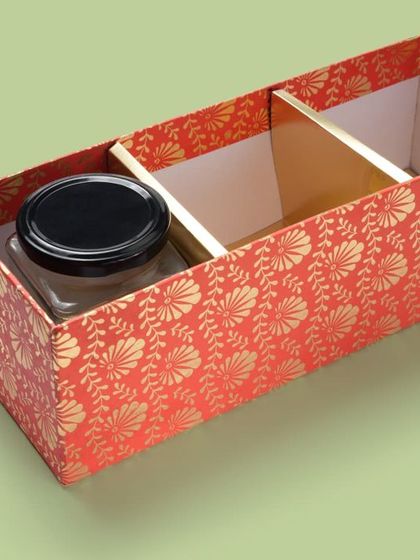 A festive red gift box with dividers, shown with a sample jar inside. This helps customers understand the size and capacity of the packaging.
