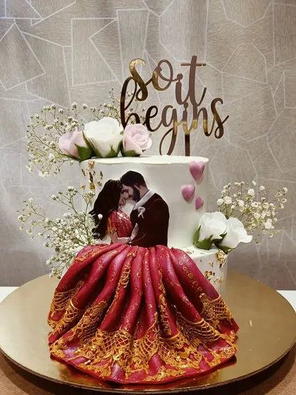 "And so it begins." This stunning engagement cake features a custom photo of the couple and an intricate, edible red gown that flows from the top tier. It's a personalized design that truly tells a story.