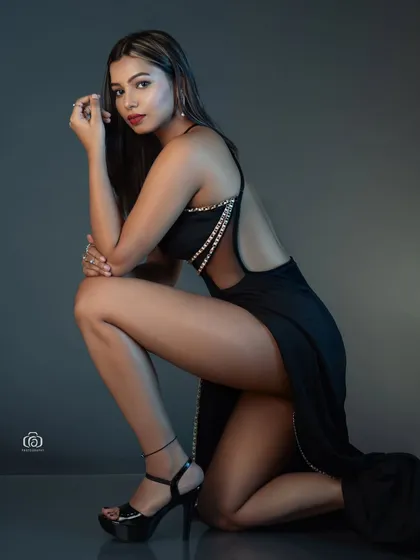 A low-angle shot that emphasizes the drama of a high-slit black gown. The lighting is focused to create a sense of intimacy and highlight the elegant lines of the dress.
