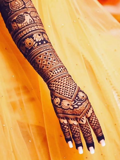 A close-up of a bridal arm against a yellow lehenga, highlighting the fine details of the lotus and elephant band, and the intricate geometric patterns.