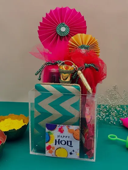 For a modern touch, I offer this acrylic box Holi hamper. It's filled with a chevron-print pouch and other colorful goodies, all visible through the clear box.