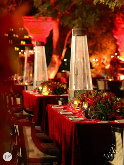 A long dining table setup with a continuous runner of red florals, creating a dramatic and luxurious tablescape for the sangeet dinner.