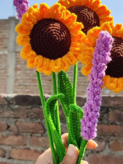 A lovely combination of handmade crochet sunflowers and lavender stems held against a brick wall, capturing the vibrant colors of spring.